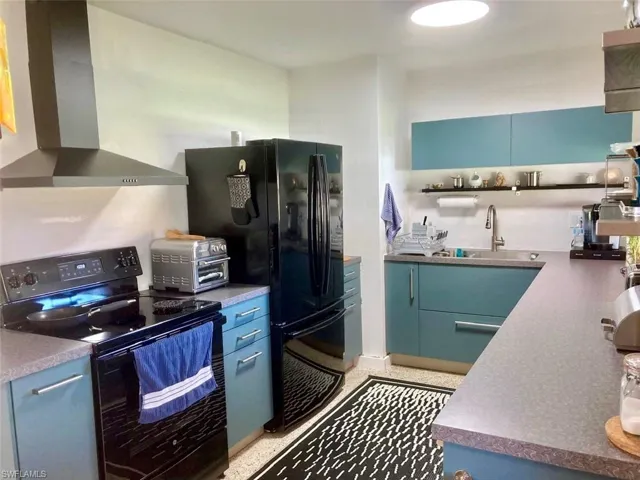 Kitchen with black appliances, wall chimney exhaust hood, blue cabinetry, and open shelves