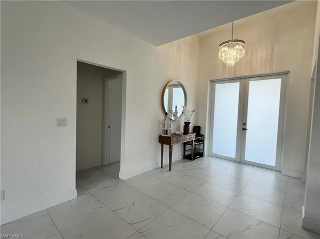 Foyer featuring light marble finish flooring, a chandelier, and french doors