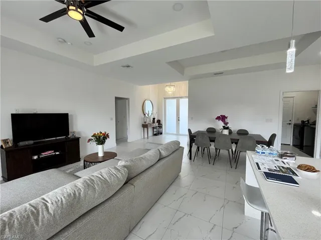 Living area with a raised ceiling, ceiling fan, and light marble finish floors