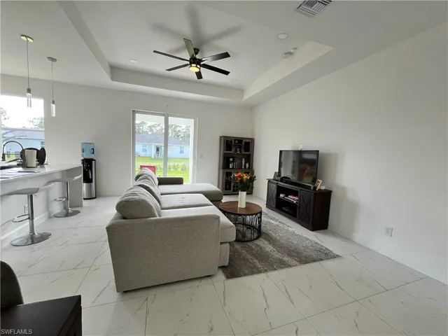 Living room with visible vents, baseboards, a raised ceiling, a ceiling fan, and marble finish floor