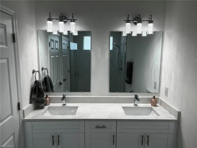 Full bath featuring double vanity, a shower stall, a textured wall, and a sink