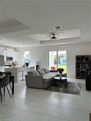Living room with a tray ceiling, a ceiling fan, visible vents, recessed lighting, and marble finish floor