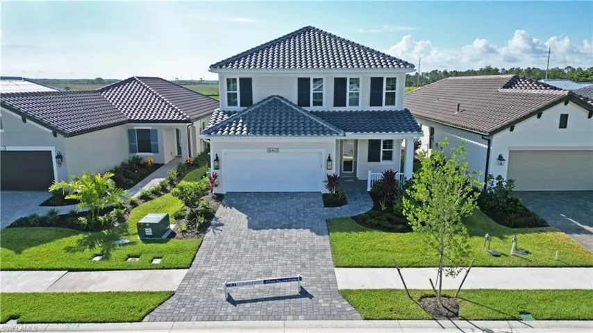 View of front of property featuring a tiled roof, an attached garage, decorative driveway, a porch, and a front lawn