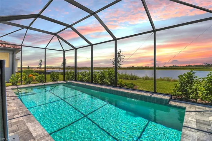 Pool at dusk featuring an outdoor pool, a sunroom, and glass enclosure