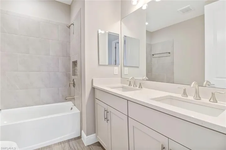 Bathroom with double vanity, bathtub / shower combination, and light wood-style flooring