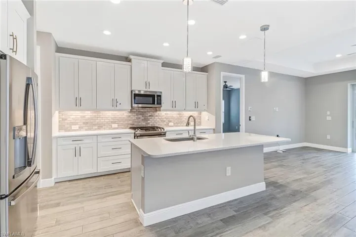 Kitchen with stainless steel appliances, white cabinets, light stone countertops, and a kitchen island with sink