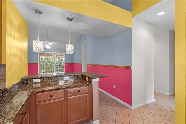 Kitchen counter with a polished granite surface, wood-finish cabinetry, and two pendant light fixtures