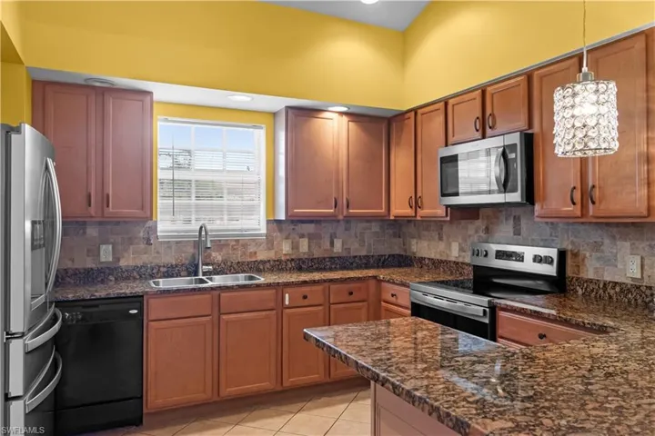 Kitchen featuring L-shaped countertops with a breakfast bar, wood-finish cabinetry, stainless steel appliances, and a tiled backsplash
