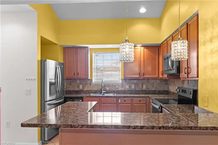 Well-appointed kitchen featuring a breakfast bar, stainless steel appliances, wood cabinetry, stone-look countertops, and decorative pendant lighting