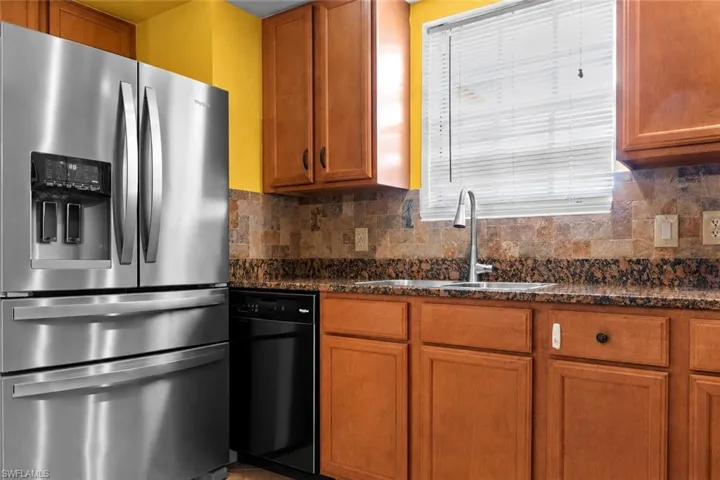 Kitchen featuring stainless steel French door refrigerator, wood cabinetry, stone countertops, and a tile backsplash