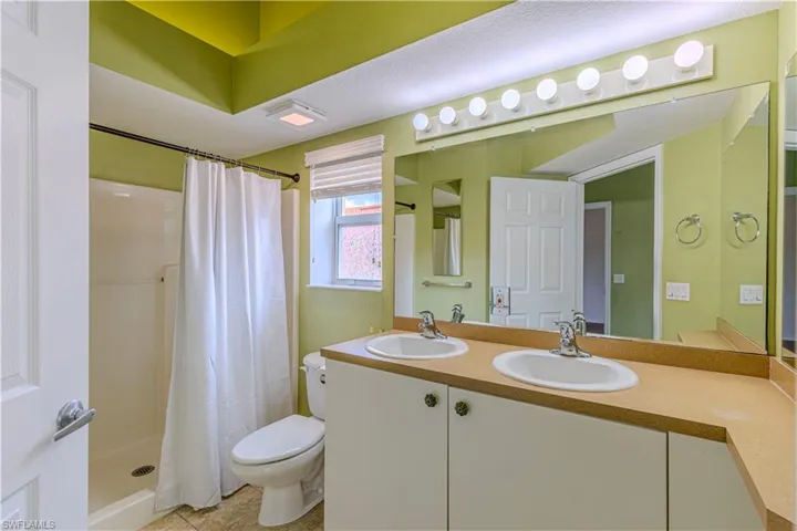 Bathroom featuring a dual vanity with light-toned countertops and undermount sinks, a large wall-mounted mirror, and overhead strip lighting