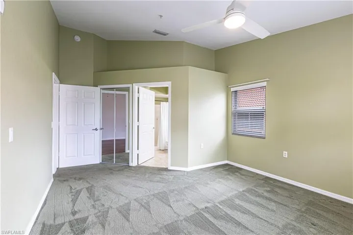 Carpeted room with a ceiling fan, window with blinds, and white paneled doors leading to another room and an en-suite bathroom