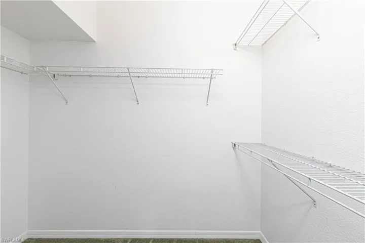 Walk-in closet featuring white wire shelving, white textured walls, and green carpet flooring