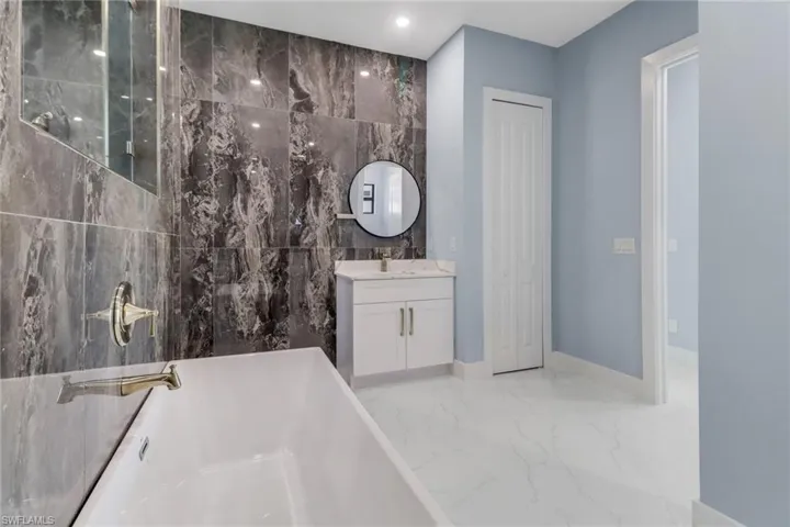 Bathroom with tile walls, vanity, marble finish floor, a soaking tub, and recessed lighting