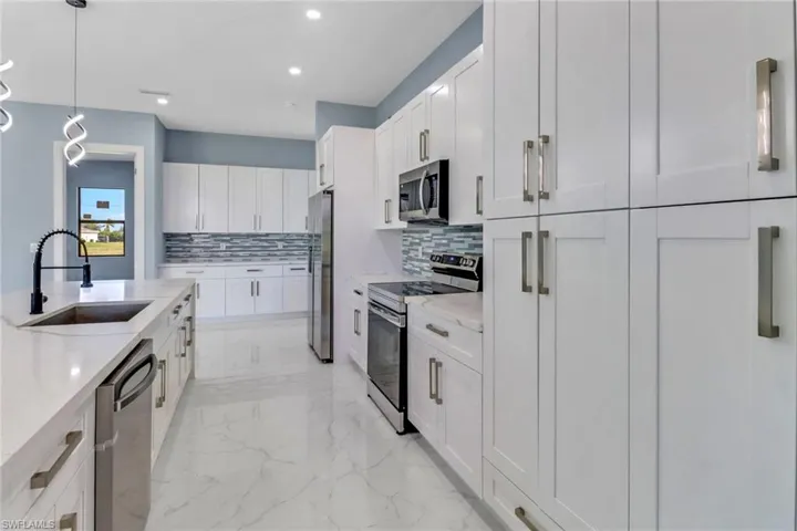 Kitchen featuring a sink, marble finish floor, stainless steel appliances, white cabinetry, and tasteful backsplash