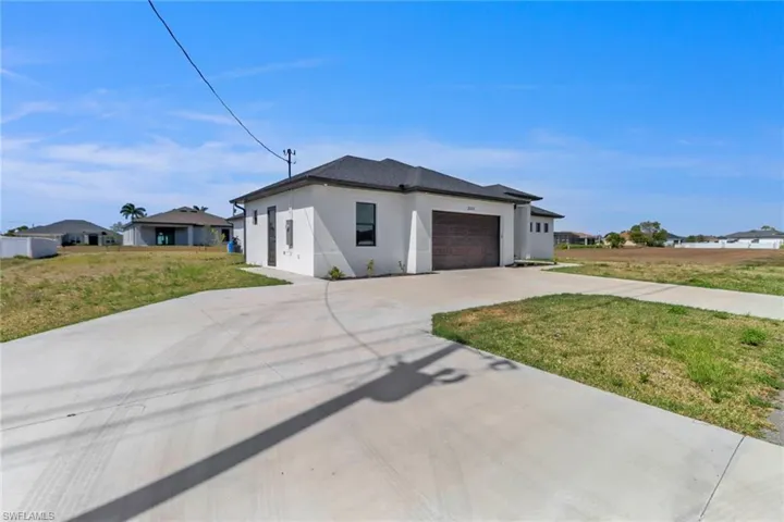 View of front of home featuring an attached garage, a front lawn, driveway, and stucco siding