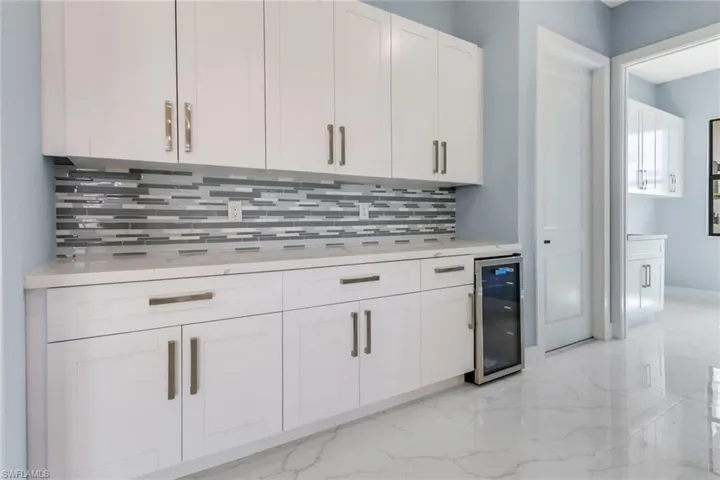 Kitchen with light countertops, marble finish floor, wine cooler, and tasteful backsplash