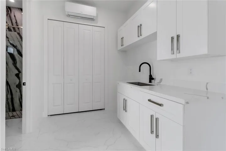 Kitchen featuring marble finish floor, light countertops, a wall mounted AC, white cabinets, and a sink