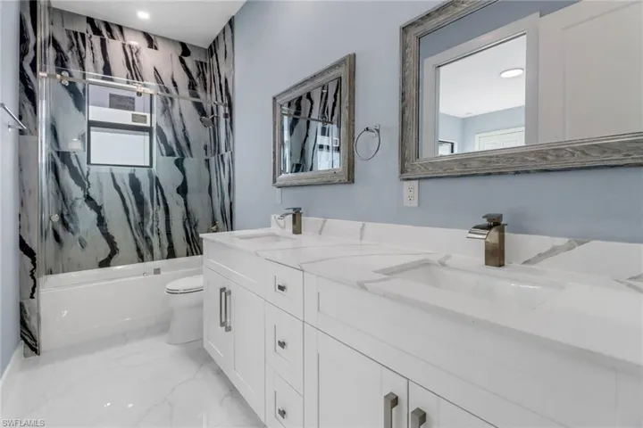 Bathroom with a sink, double vanity, toilet, marble finish floor, and shower / bathing tub combination