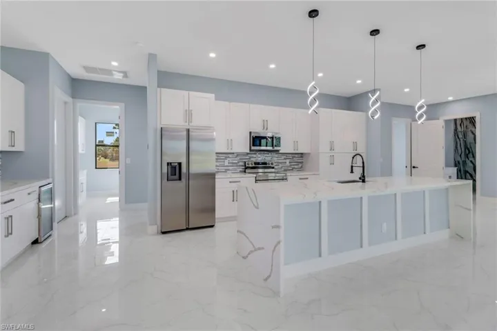Kitchen featuring decorative backsplash, a kitchen island with sink, white cabinets, a sink, and appliances with stainless steel finishes
