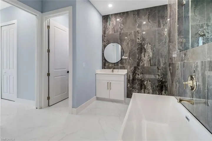 Bathroom featuring vanity, marble finish floor, a washtub, baseboards, and recessed lighting