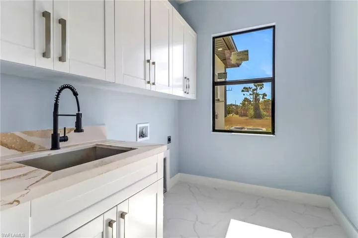 Laundry area with electric dryer hookup, cabinet space, a sink, baseboards, and marble finish floor