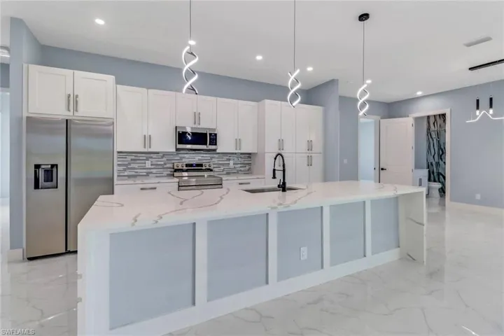 Kitchen with decorative backsplash, a large island with sink, a sink, marble finish floor, and stainless steel appliances