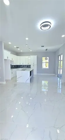 Kitchen featuring a kitchen island, sink, white cabinets, decorative backsplash, and light stone countertops