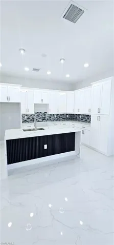 Kitchen with white cabinetry, an island with sink, and hanging light fixtures