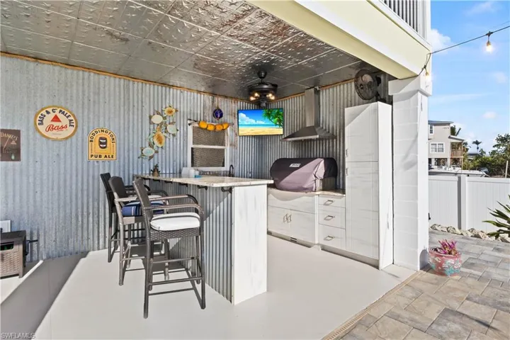 An outdoor kitchen with hardy designer cabinets, granite counters, a grill, TV, and galvanized ceiling offers the perfect setting for hosting guests.