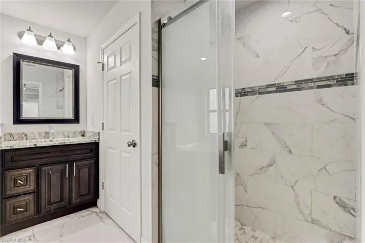 Shower enclosure featuring a sliding glass door and large format marble-look tile walls with a mosaic accent band
