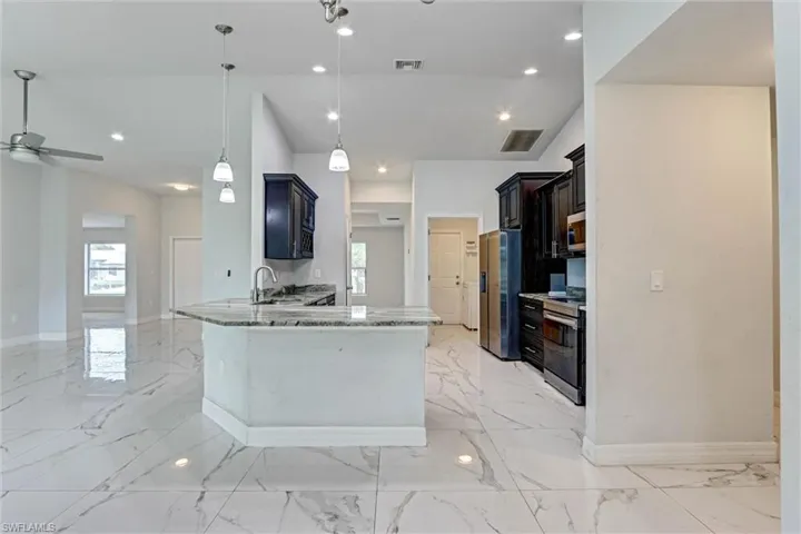 Open-concept living space featuring high ceilings, recessed lighting, a kitchen island with stone countertops, dark wood cabinetry, and large format marble-look tile flooring
