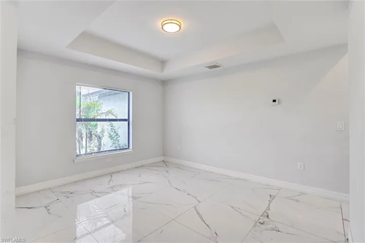 Spacious room featuring large format tile flooring, a tray ceiling, and a prominent window