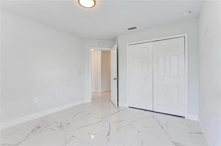 Spacious room featuring white walls, bi-fold closet doors, and white marble-look tile flooring