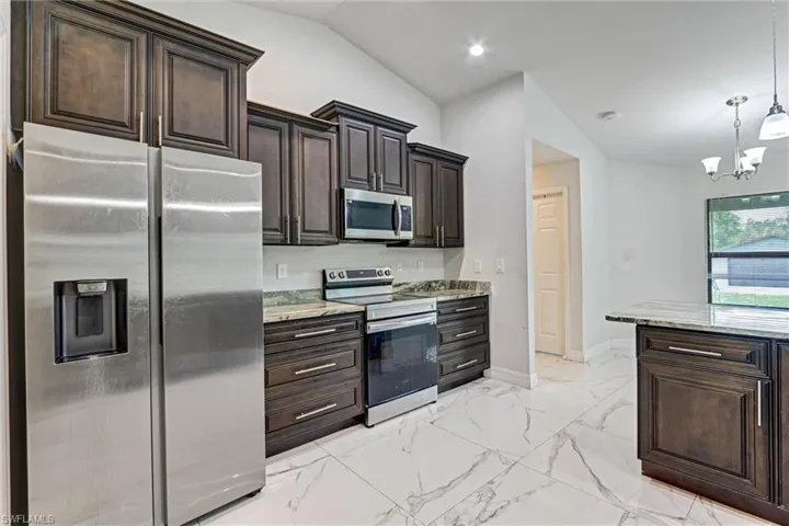 Kitchen featuring dark wood cabinetry, stainless steel appliances, granite countertops, and large format tile flooring
