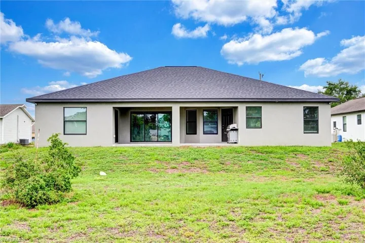 Rear exterior featuring a grey shingle roof, light-colored stucco siding, and black-framed windows