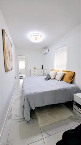 Bedroom featuring an AC wall unit, light marble finish flooring, and baseboards