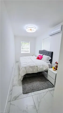 Bedroom featuring a wall mounted air conditioner, marble look tiles, and baseboards