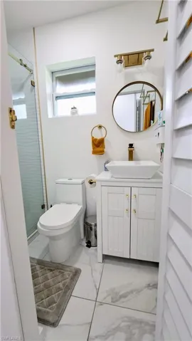Full bathroom featuring marble look tile flooring, a shower stall, toilet, and vanity