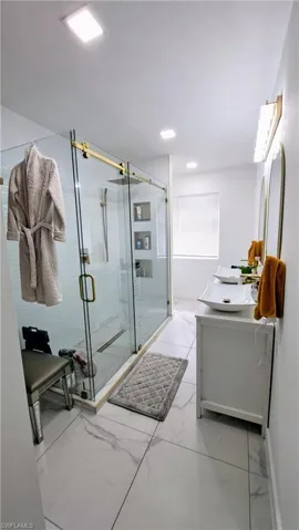 Full bath with vanity, marble look tile flooring, a stall shower, and baseboards