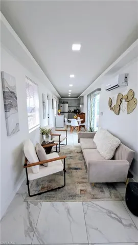 Living area with marble look tiles, a wall mounted AC, and baseboards