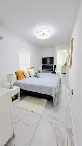 Bedroom featuring light marble finish flooring, baseboards, and a wall mounted AC