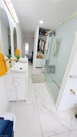 Bathroom featuring marble look tiles, vanity, a shower stall, and a spacious closet