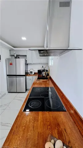 Kitchen with freestanding refrigerator, ventilation hood, black electric stovetop, a sink, and light marble finish flooring