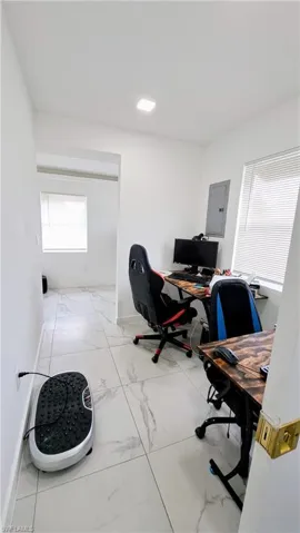 Home office featuring light marble finish floors, electric panel, and baseboards