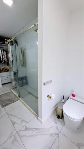 Bathroom featuring marble finish flooring, a stall shower, toilet, a spacious closet, and baseboards