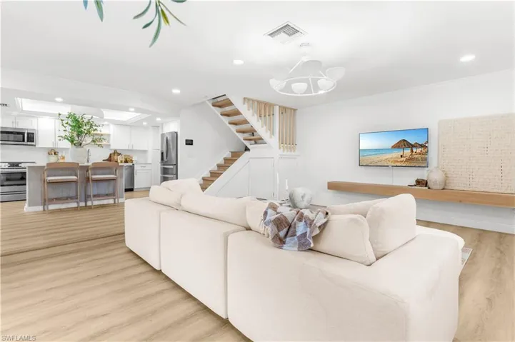 Living room featuring sink, light wood-type flooring, crown molding, and an inviting chandelier