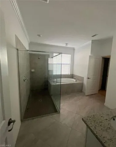 Bathroom with a garden tub, a shower stall, ornamental molding, vanity, and light tile patterned floors
