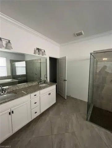 Full bathroom with double vanity, a stall shower, and ornamental molding