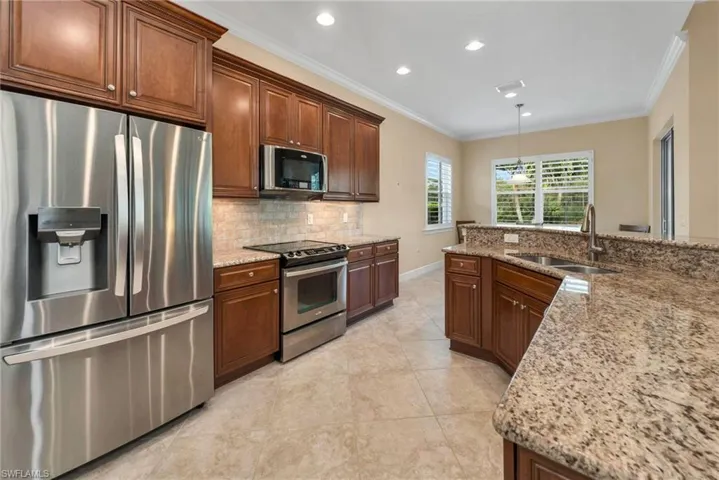 Kitchen featuring light stone counters, appliances with stainless steel finishes, crown molding, and sink